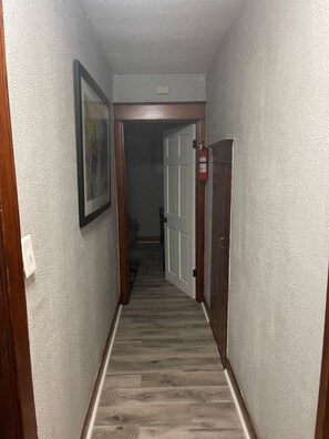 A hallway with a wooden door, a fire extinguisher, and a framed picture on the wall.