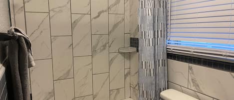 Une salle de bain avec une douche, des toilettes et une fenêtre avec des stores.