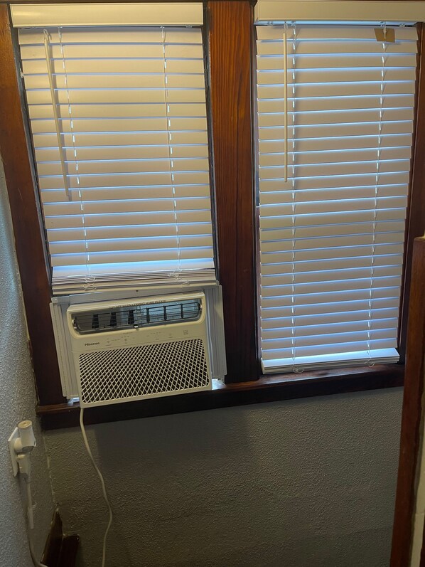 A window with blinds partially open, revealing a Hisense air conditioner unit below.