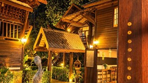 Uma cabana de madeira com uma estátua de pedra, galeria coberta e um pequeno jardim.