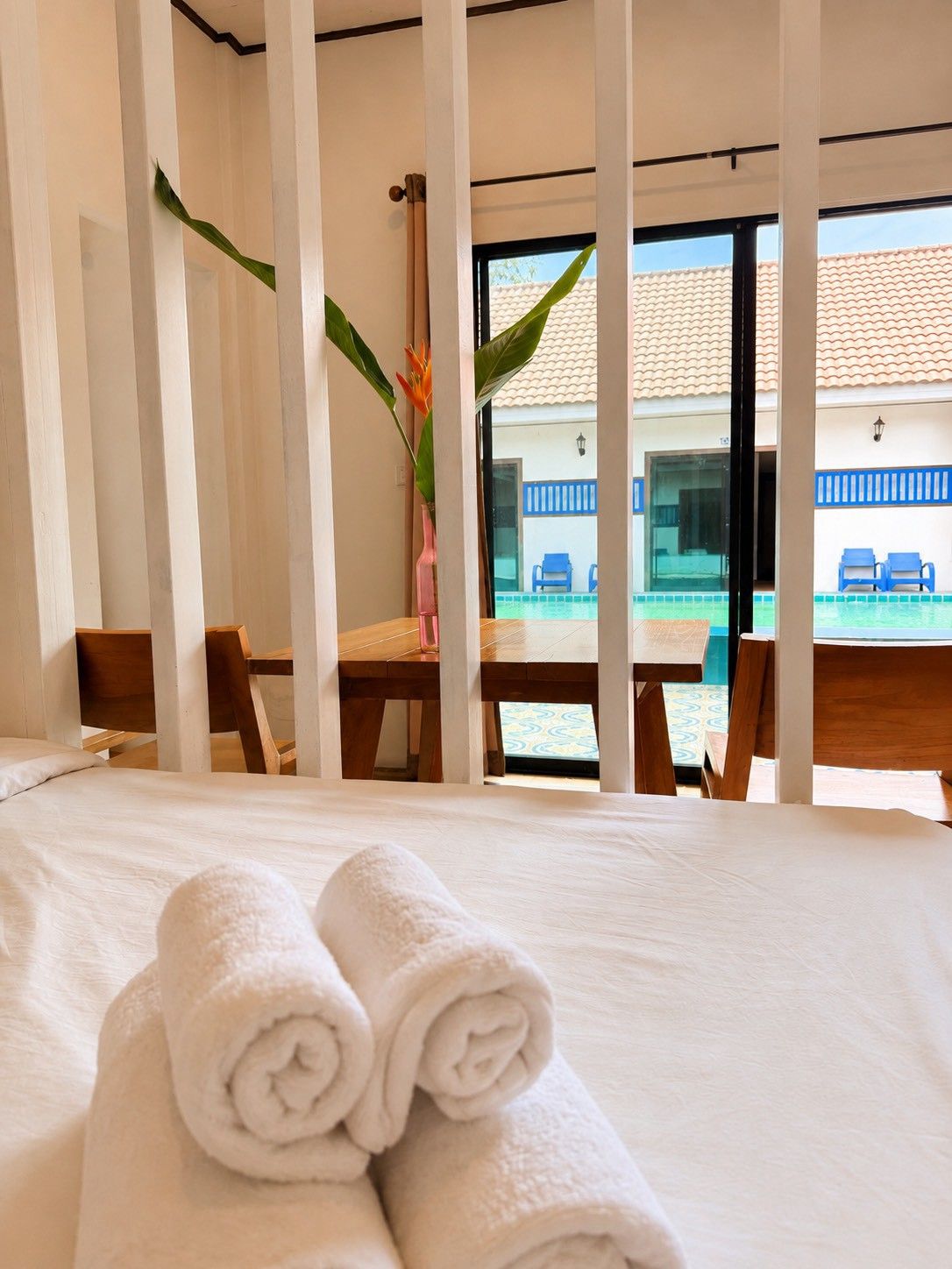 Een hotelkamer met een bed, een tafel, stoelen, een raam met uitzicht op een zwembad en een gebouw, en een plant.