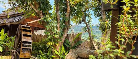 A traditional water wheel, lush greenery, and a wooden structure with a thatched roof.