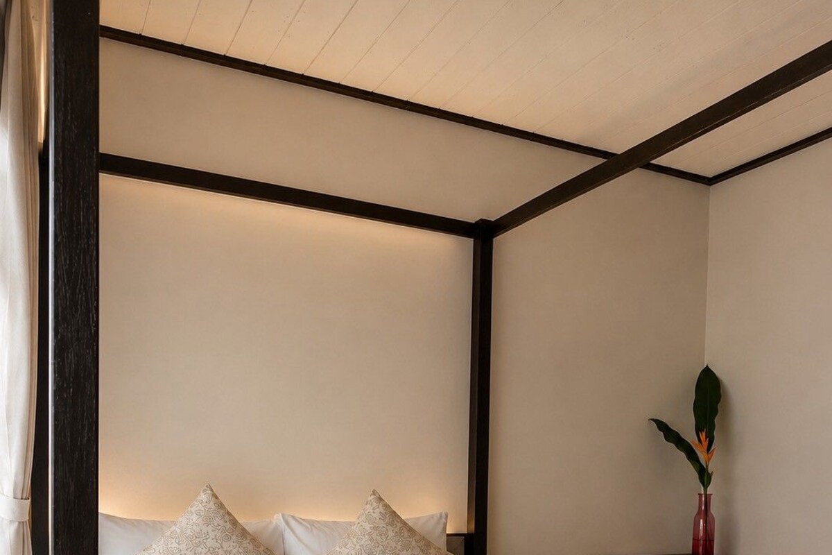 A neatly made bed with white linens and rolled towels, a small wooden table with a vase, and a chair.
