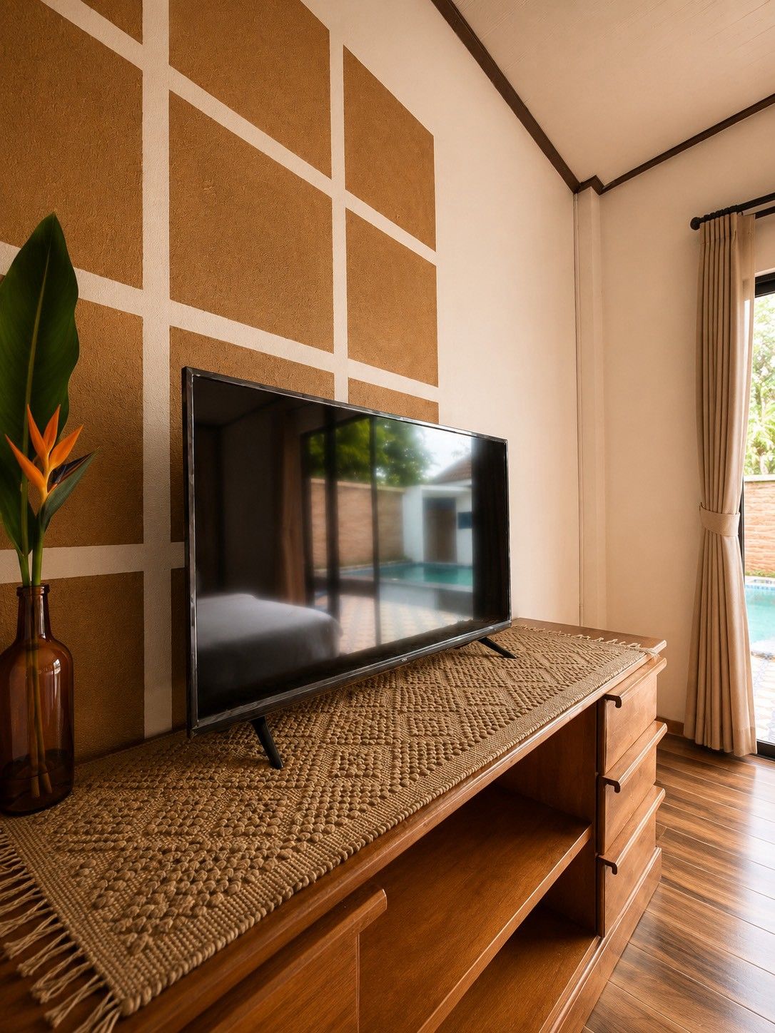 Televisão de tela plana em prateleira de tecido, uma planta e vista de uma piscina pela janela.