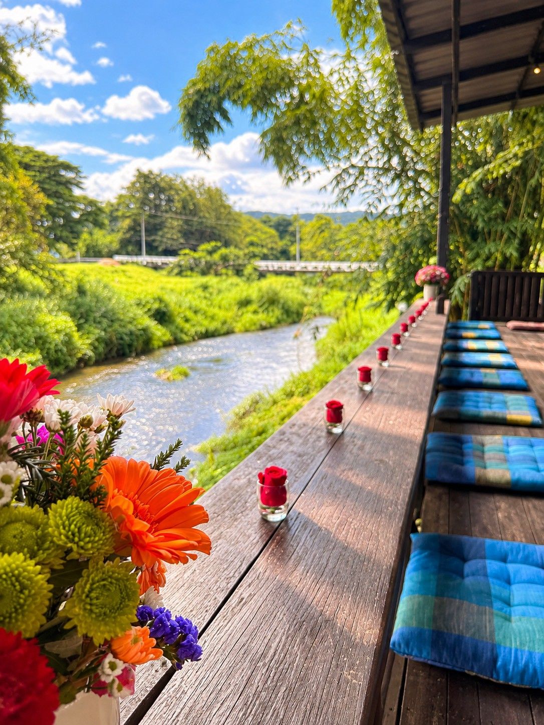 A wooden deck with a river view, benches, and small vases with flowers.