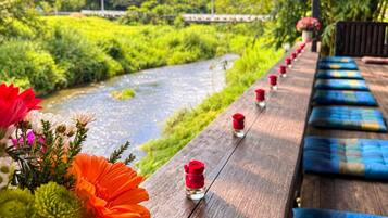 A wooden deck with a river view, benches, and small vases with flowers.
