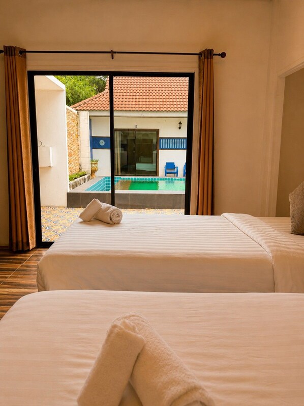 A hotel room with two beds, a view of a pool, and a sliding glass door leading to an outdoor area.