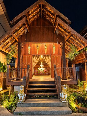 A wooden structure with a central statue, steps leading up to it, and two lion statues at the entrance.