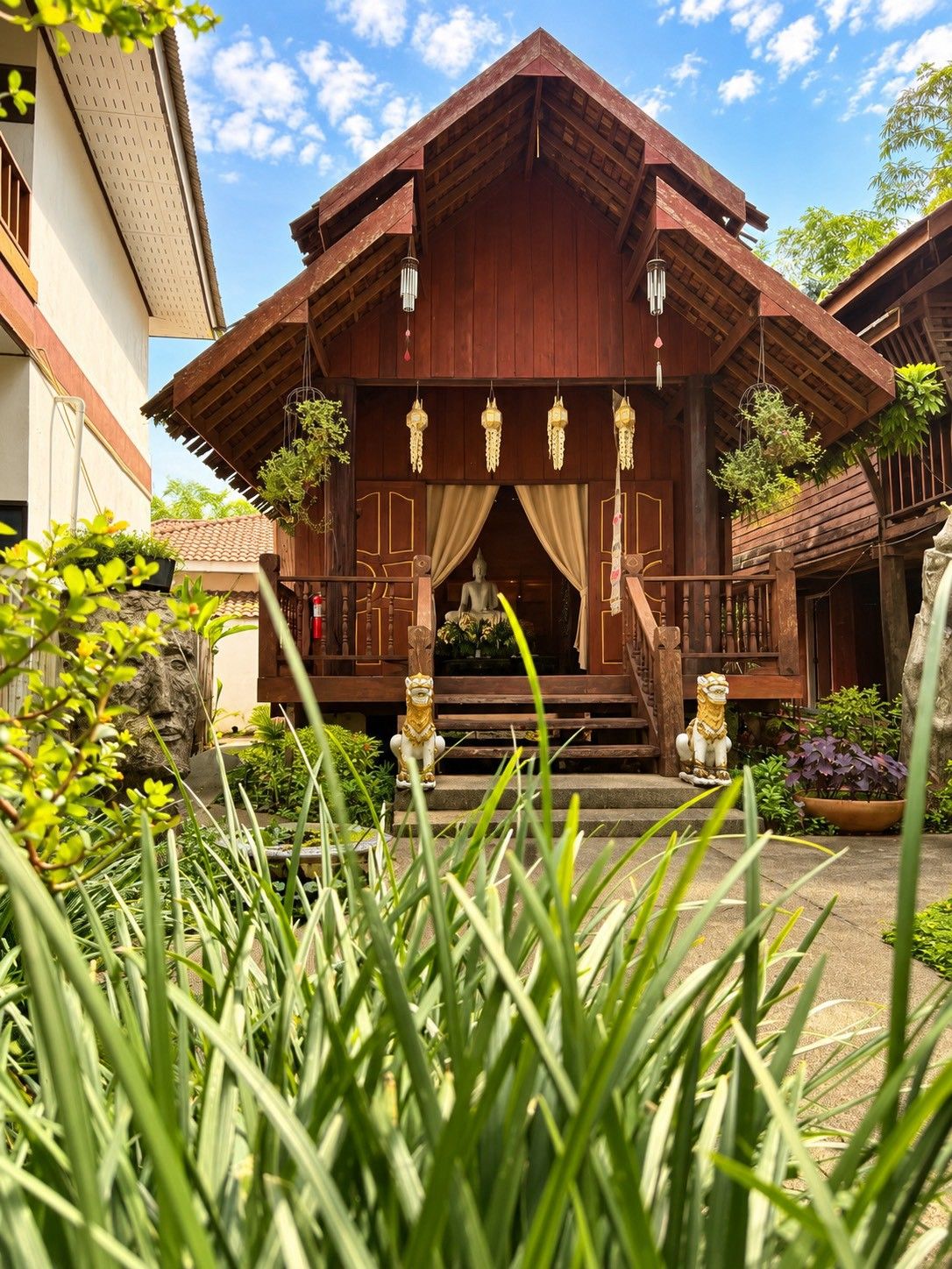 A traditional wooden building with a porch, a Buddha statue, and decorative hanging lanterns.