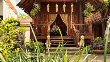 A traditional wooden building with a porch, a Buddha statue, and decorative hanging lanterns.