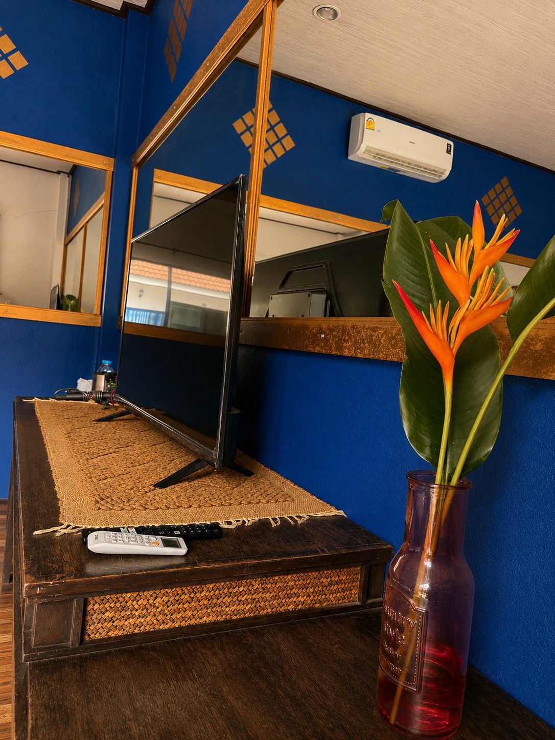 A room with a television on a wooden stand, a remote control, a vase with a plant, and a wall-mounted air conditioner.