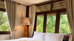 Quarto de hotel com uma cama grande, abajur e janela com cortinas.