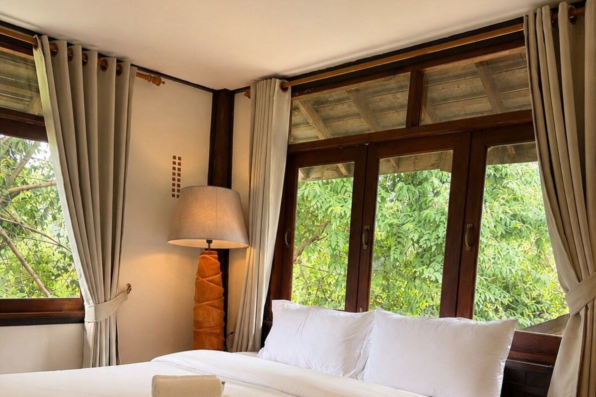 A hotel room with a large bed, a bedside lamp, and a window with curtains.