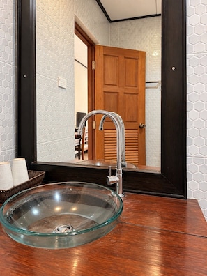 A bathroom with a glass bowl sink, a wooden door, and a mirror reflecting the room. - Chaba Varee Resort Doi Saket Chiang Mai (Pa Meung)