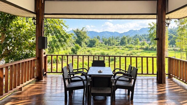 Área de estar coberta ao ar livre, com mesa e cadeiras, oferecendo vista para uma paisagem exuberante com montanhas.