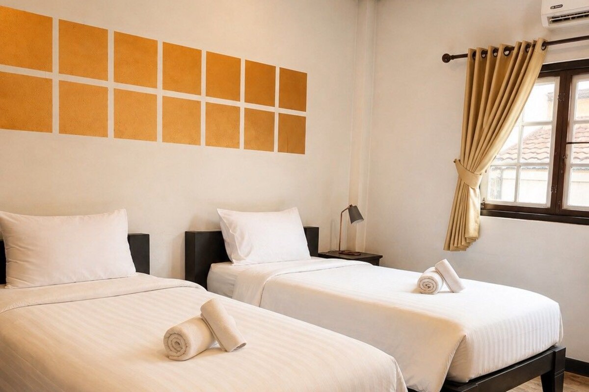 A hotel room with two beds, a window with curtains, and a wall with a geometric pattern.