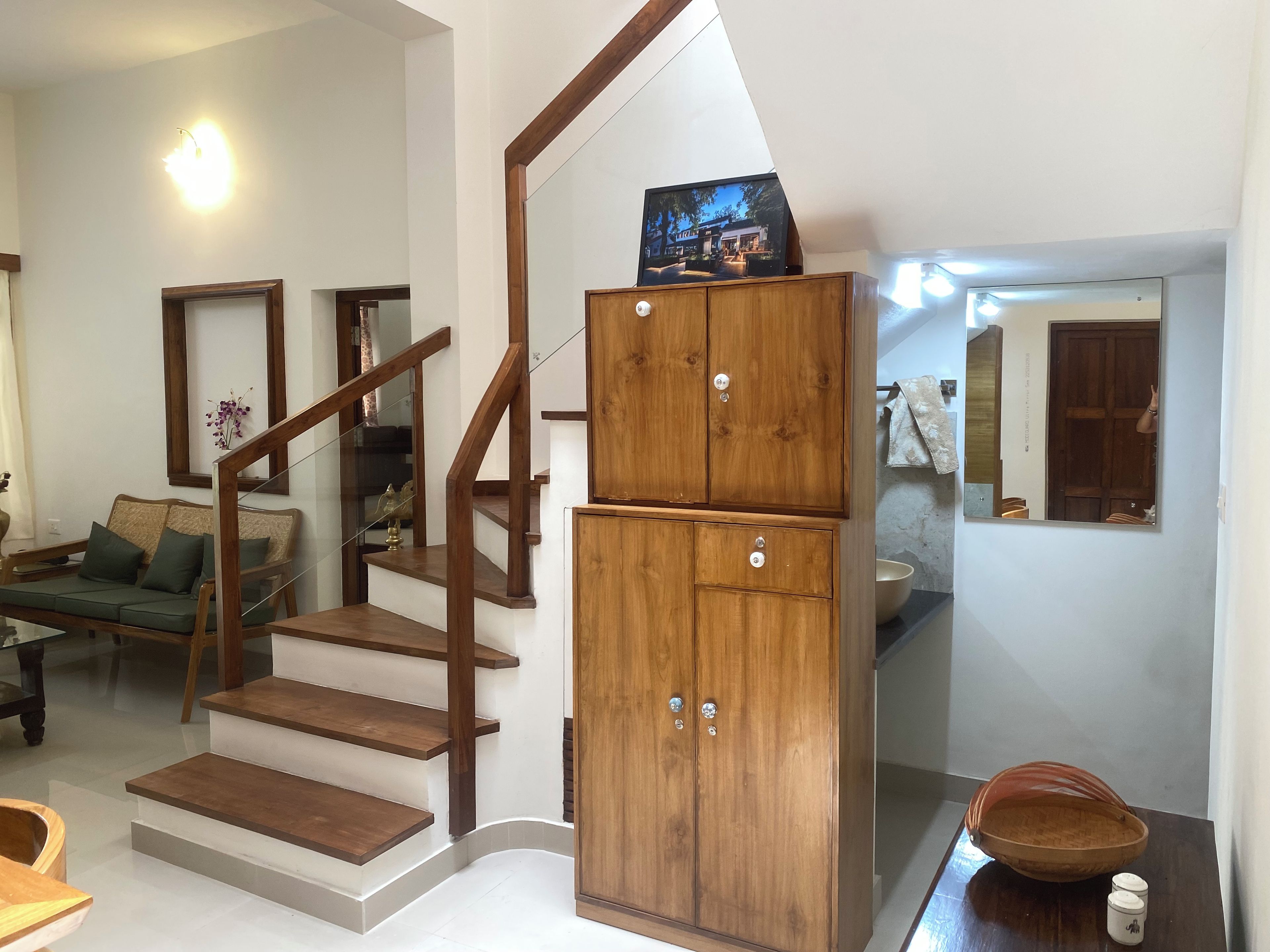 Un escalier avec des rampes en bois menant à un palier, un canapé, un meuble sur lequel est posée une télévision, et un coin repas avec une table et des chaises.