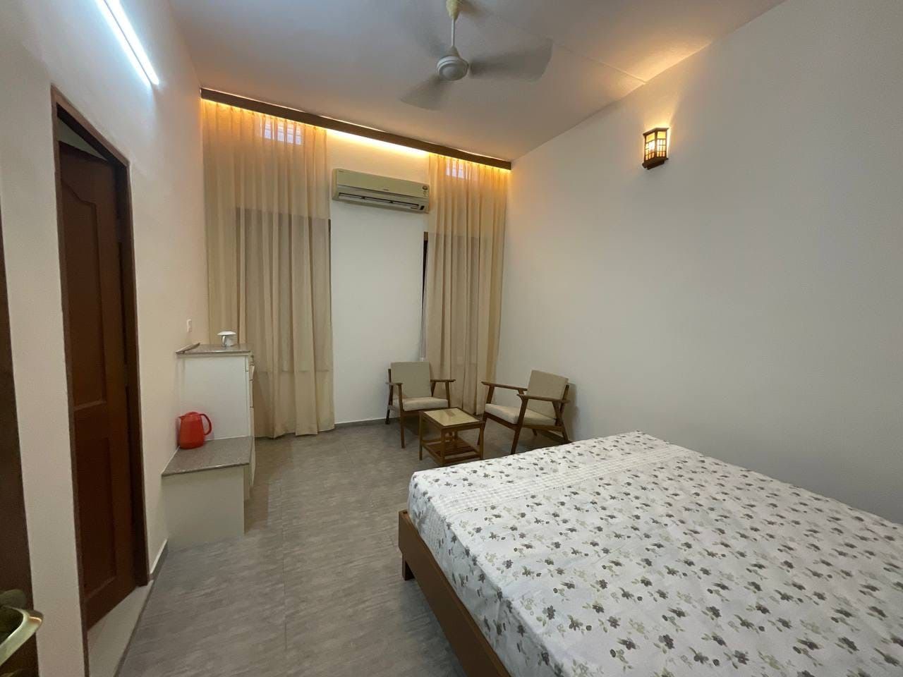 Une chambre à coucher comprenant un lit, un bureau, une chaise, un appareil de climatisation et une fenêtre avec des rideaux.