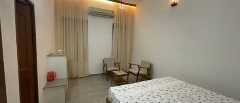 A bedroom with a bed, a desk, a chair, an air conditioning unit, and a window with curtains.