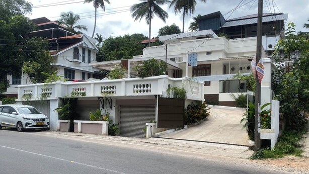 Edifício residencial com portão fechado, entrada de automóveis e um carro branco estacionado na frente.