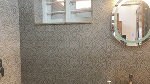 Casa de banho com papel de parede estampado, um espelho redondo, uma pia e um chuveiro.