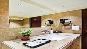 A bathroom with a large mirror, a sink, a potted plant, and two hair dryers mounted on the wall. - Suite Hotel Urban Oasis (Pune)