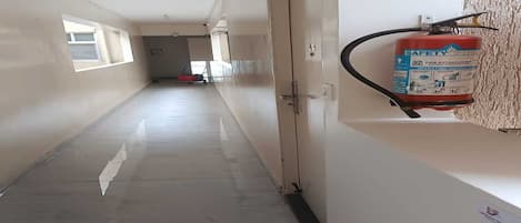 A corridor with a fire extinguisher mounted on the wall, a door at the end, and a window on the left.