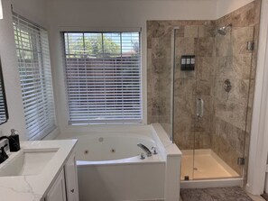 Un baño moderno con una bañera independiente, una ducha con mampara de vidrio y una ventana con persianas.