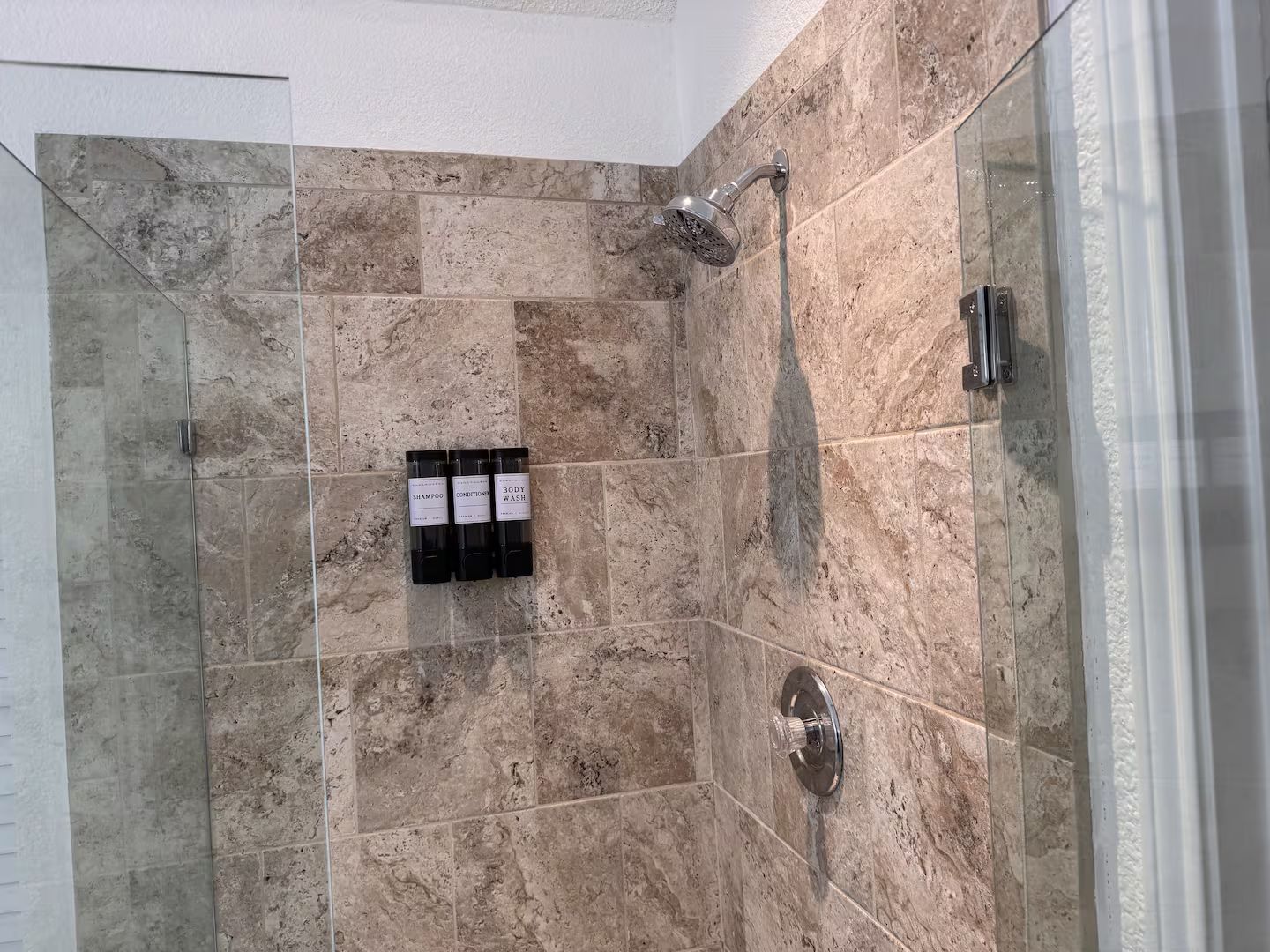A shower area with a glass door, a handheld showerhead, and a wall-mounted control panel.