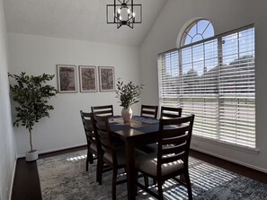 Un comedor con una mesa, sillas, una planta en maceta y cuadros en la pared.