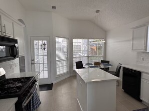 A modern kitchen with a central island, white cabinetry, and a dining area with a table and chairs.