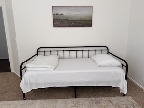 A single bed with a metal frame, white bedding, and a picture on the wall above.