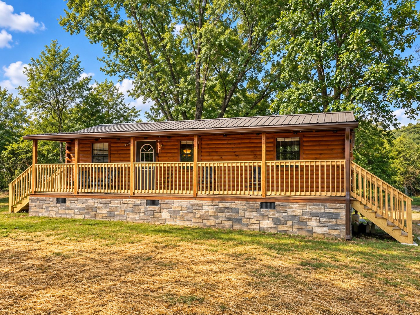 A log cabin with a stone foundation, wooden deck, and a covered porch.