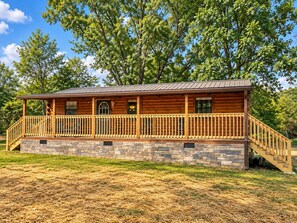 Een vakantiehuis in blokhutstijl met een stenen fundering, een houten terras en een overdekte veranda.