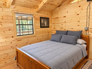 Een slaapkamer met houten lambrisering, een bed, een raam en een ingelijste foto aan de muur.
