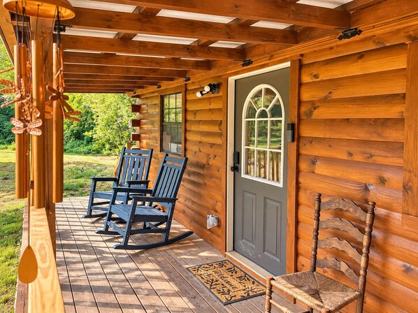 A wooden cabin with a porch, rocking chairs, and a door with a window.