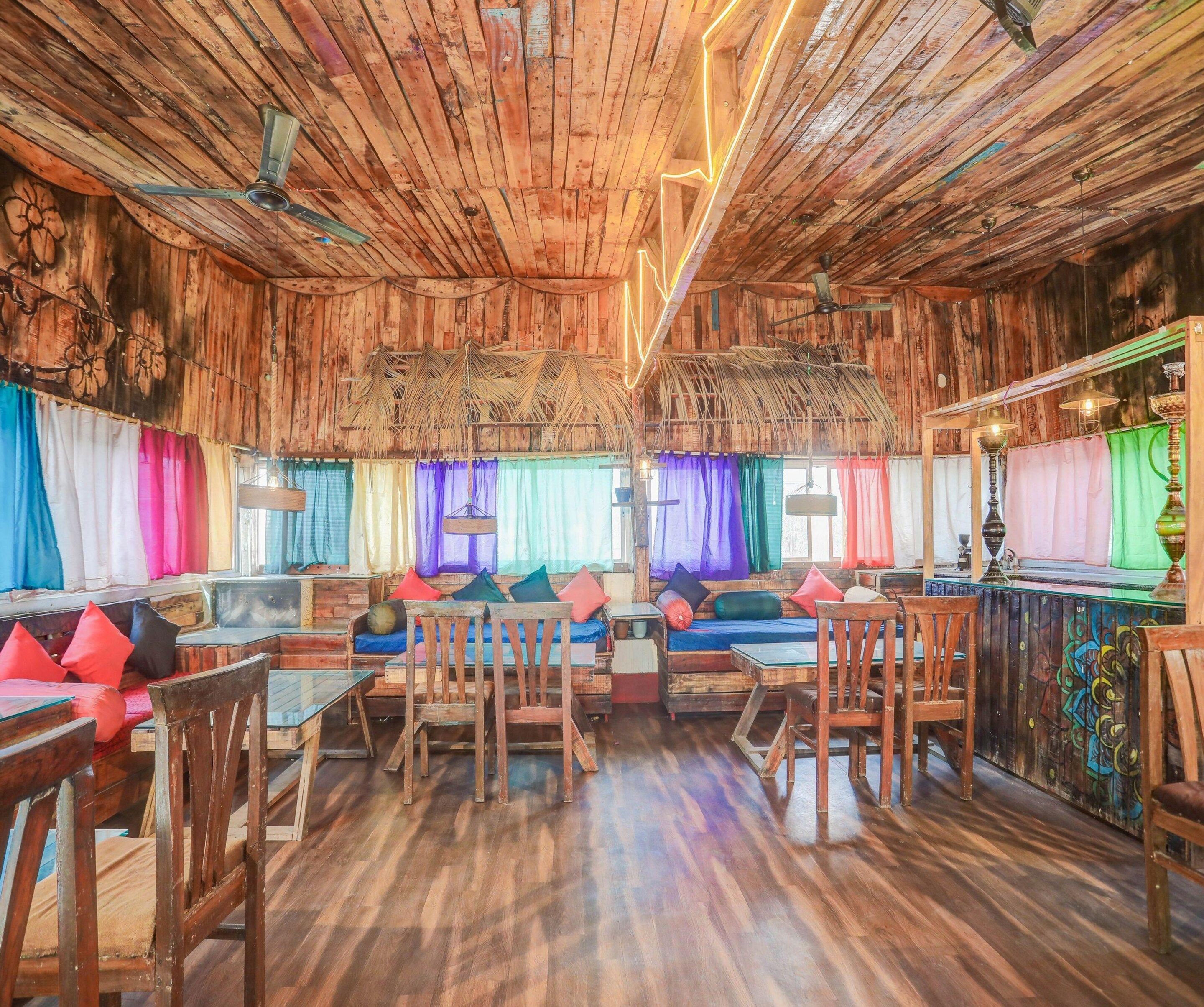 A rustic interior with wooden walls, a wooden floor, and a seating area with cushions and chairs.