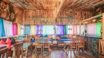 A rustic interior with wooden walls, a wooden floor, and a seating area with cushions and chairs.