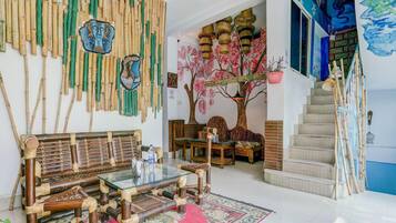 A room with a traditional bamboo wall, a sofa set, a glass coffee table, a staircase, and a painting.