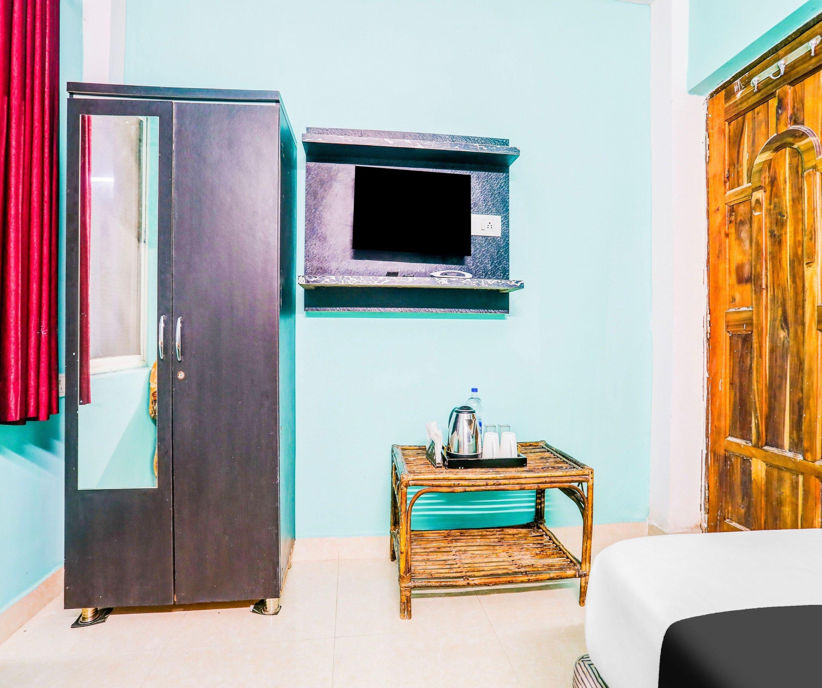 A room with a wardrobe, a television mounted on the wall, and a small table with a kettle and cups.