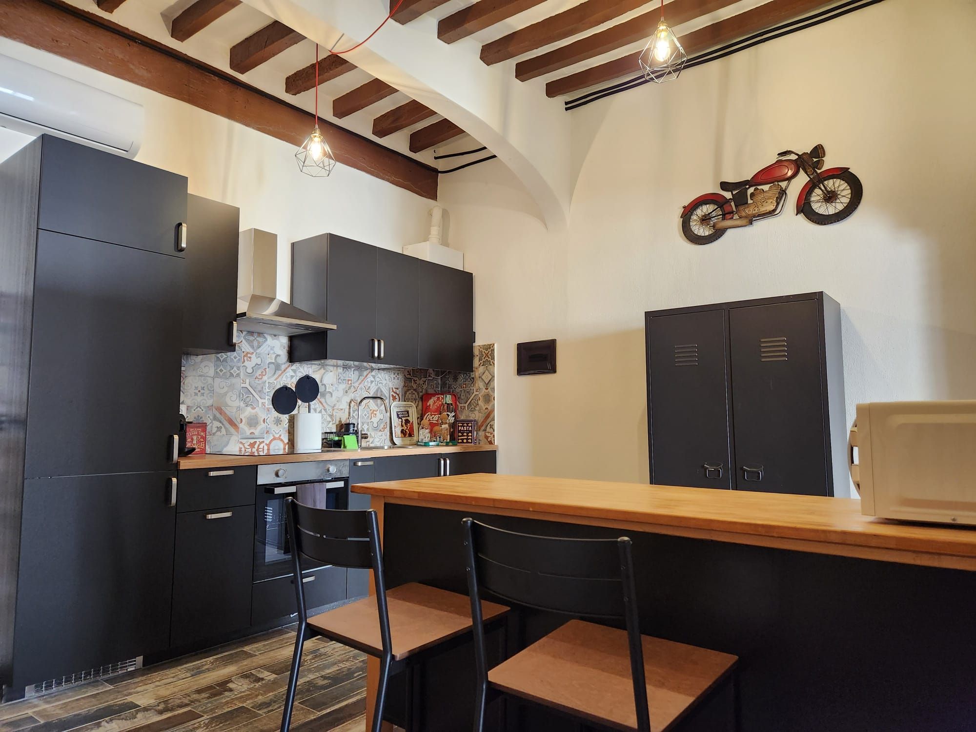 A compact kitchen with dark cabinets, a wooden countertop, two chairs, and a motorcycle decoration on the wall.