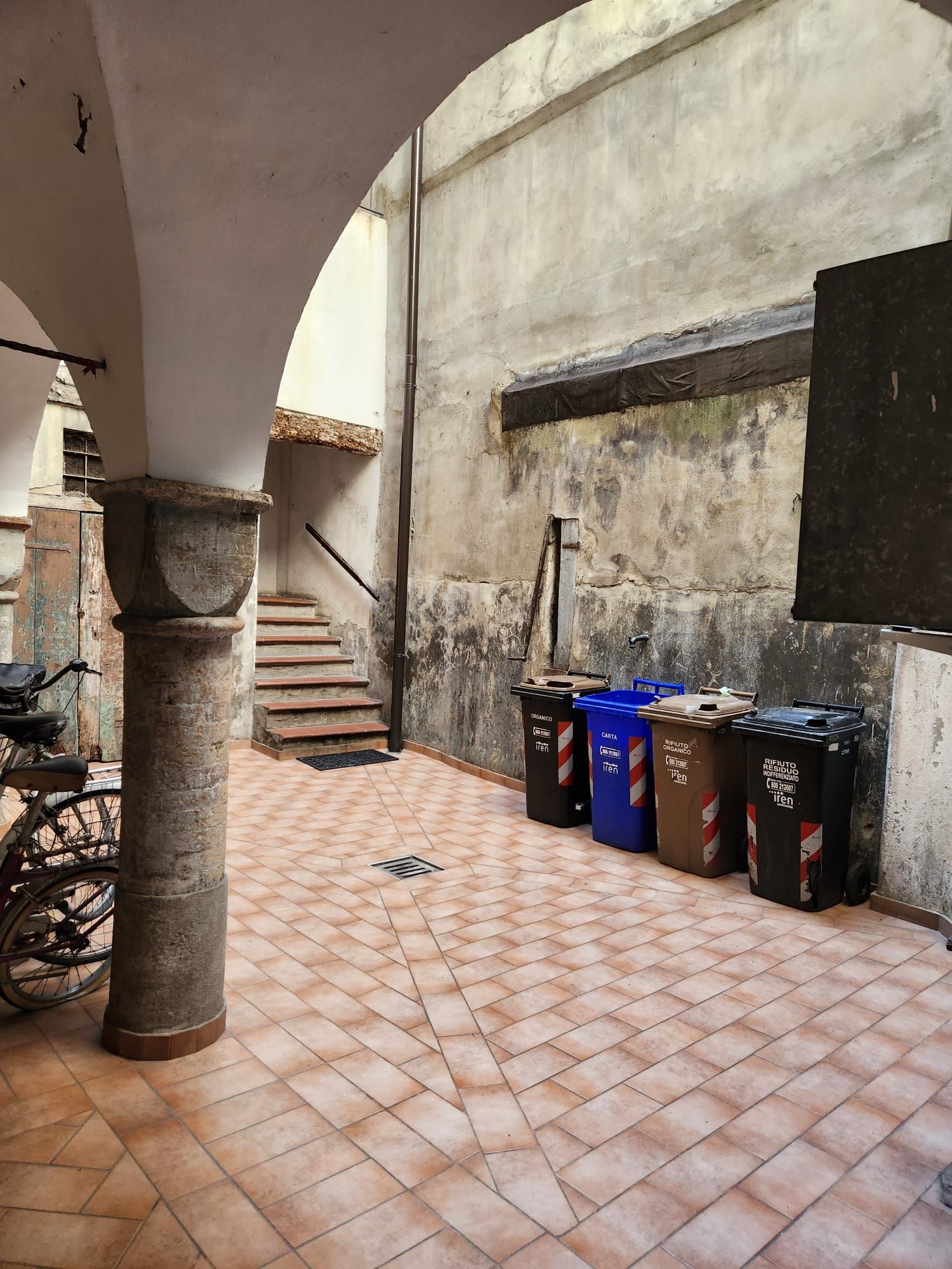 Un patio con suelo de baldosas, una escalera y contenedores de basura.