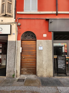 Facciata di un edificio con una porta in legno, una finestra con persiane e una targa con del testo.
