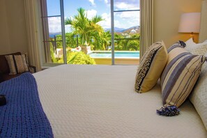 A hotel room with a large bed, a view of a swimming pool, and a balcony with palm trees. - 3-bedroom East End Villa with Pool & amazing views of the BVI islands & St John (St Thomas)
