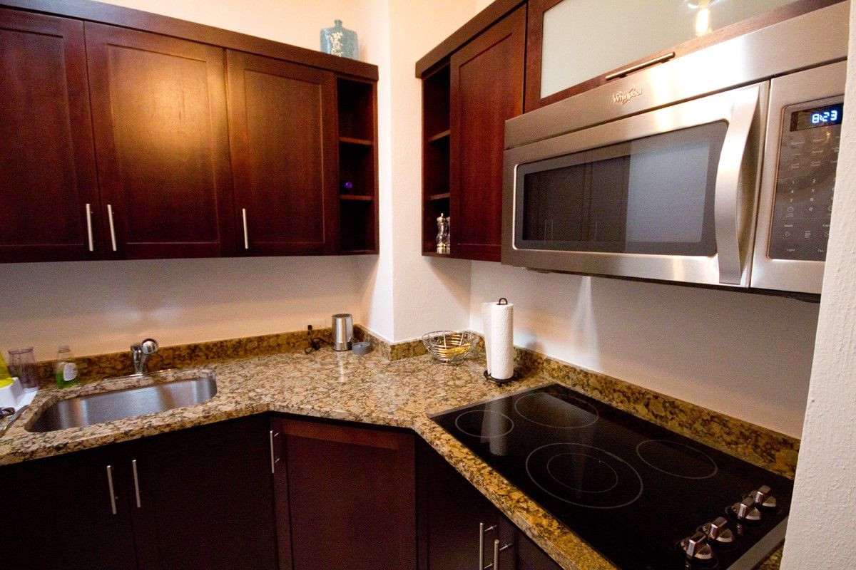 Una cocina con gabinetes de madera oscura, encimera de granito, microondas de acero inoxidable y estufa negra.