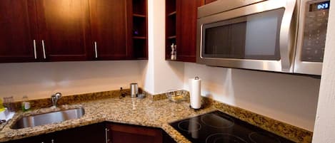 Una cocina con gabinetes de madera oscura, encimera de granito, microondas de acero inoxidable y estufa negra.