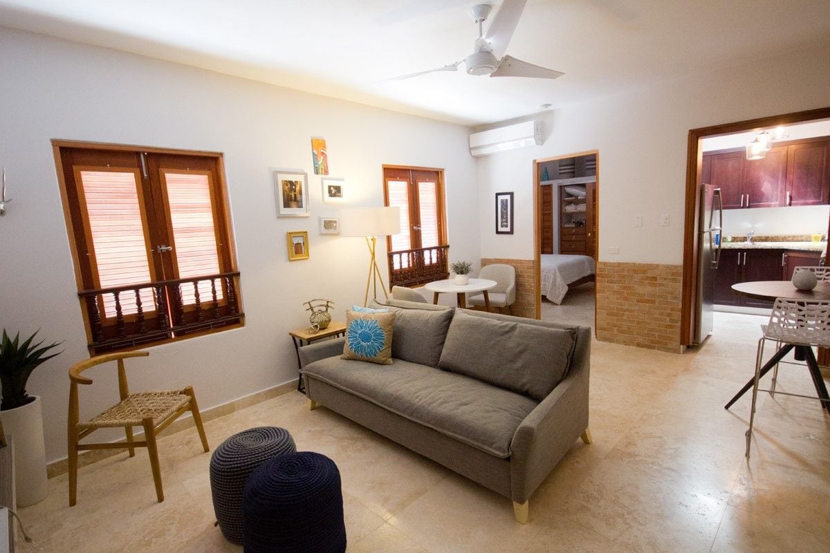 Una sala de estar con sofá, sillón, una mesita y ventilador de techo.