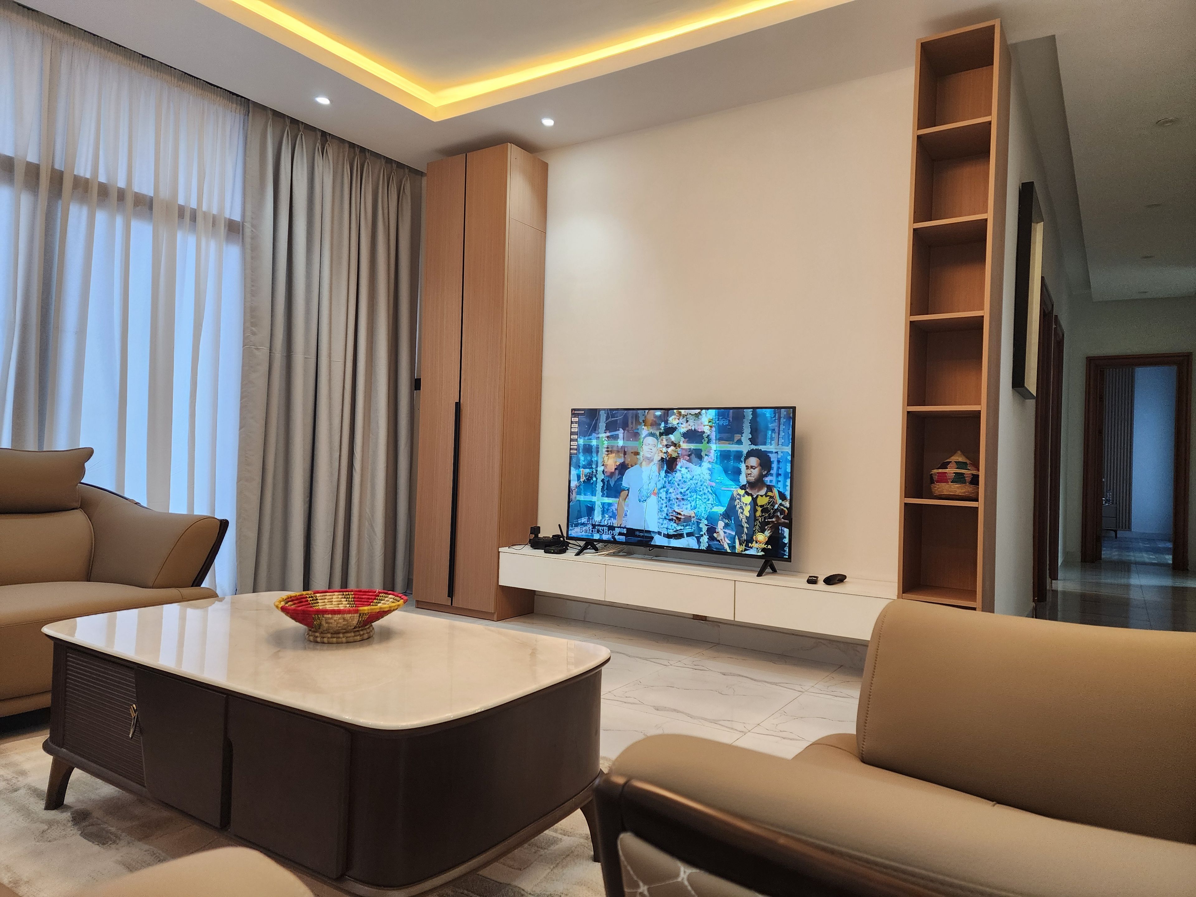 A modern living room with a flat-screen TV, leather sofas, a marble coffee table, and a wooden entertainment unit.