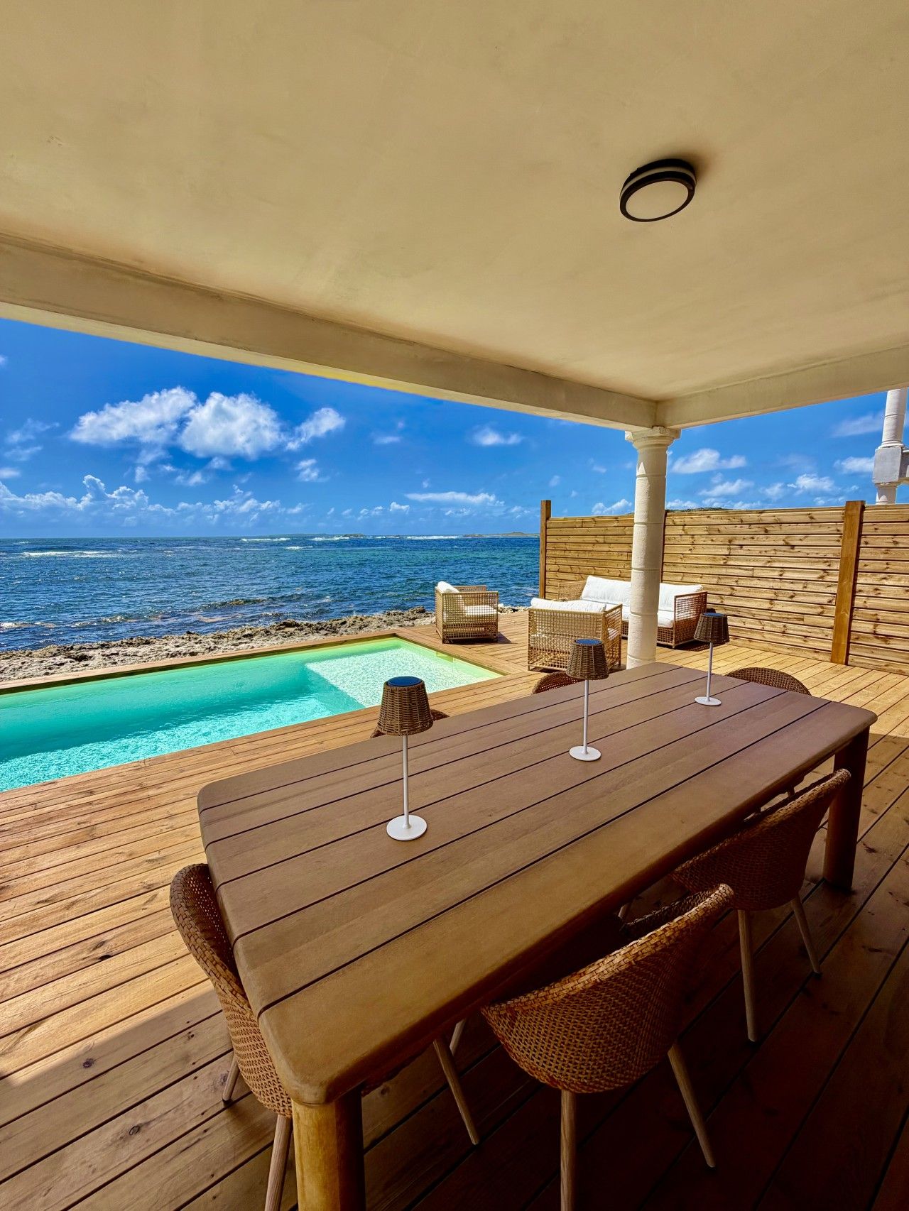 Une terrasse en bois avec une piscine, des chaises longues et une table avec des parasols.
