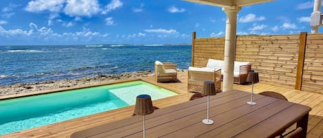 Une terrasse en bois avec une piscine, des chaises longues et une table avec des parasols.
